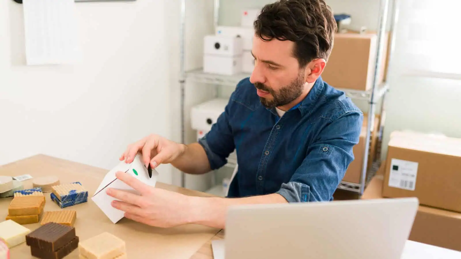 Shopinhaber geht am Schreibtisch mit Paketen seine Bestellungen durch, bevor sich aus Shopify Rechnungen versenden lassen
